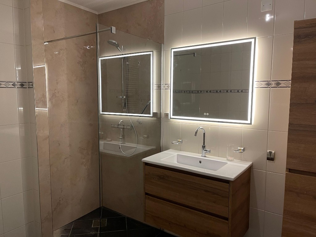 Gerenoveerde badkamer met zwevende wastafel, verlichte spiegel en douchewand
